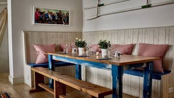 A dining area with a wooden table set for four, benches with red and white checkered cushions, and a wall-mounted surfboard.
