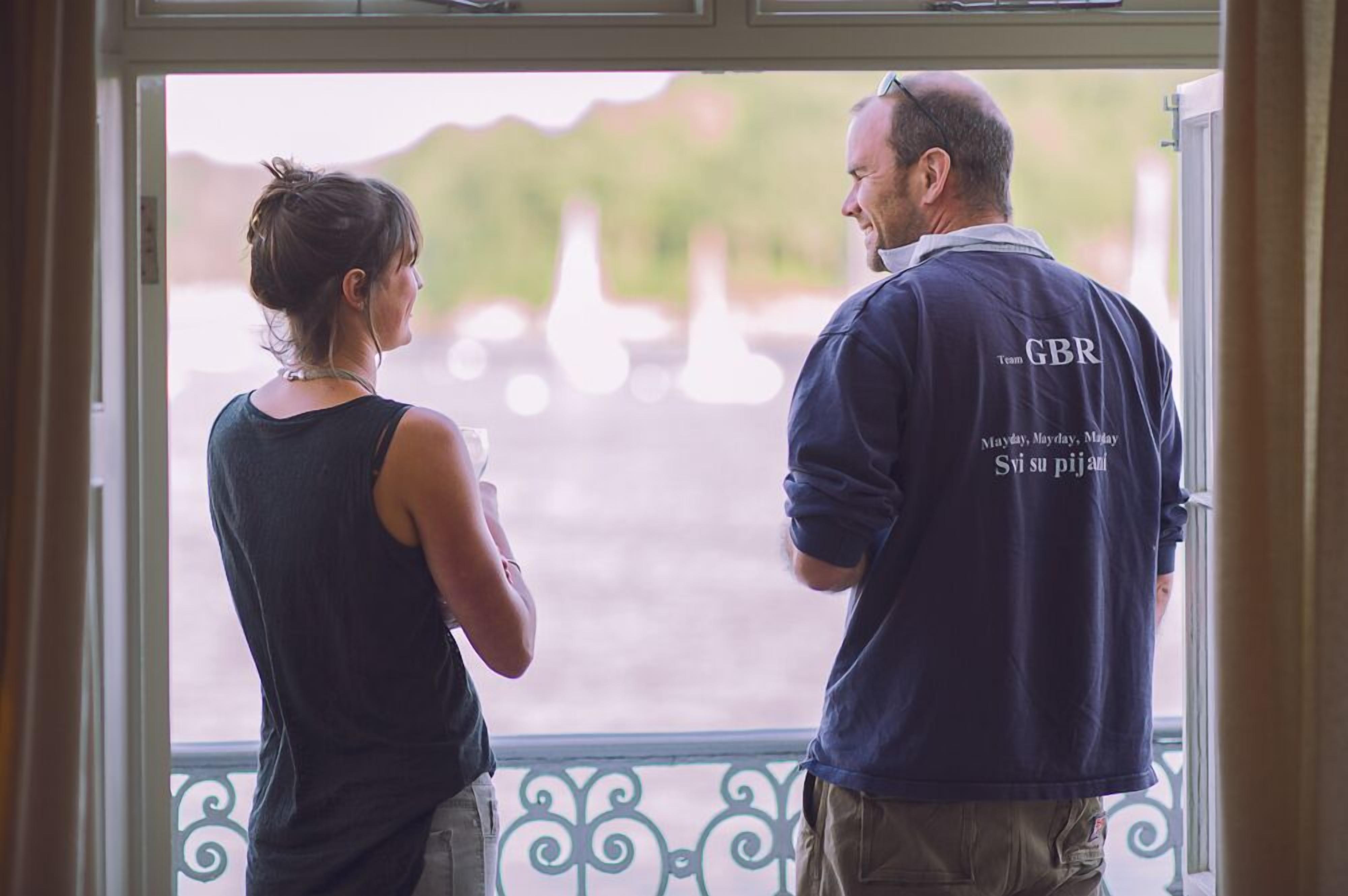 Un homme et une femme se tiennent près d’une fenêtre, d’où l’on peut voir un plan d’eau et de la verdure.