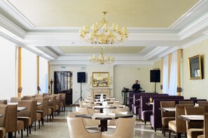 Un comedor amplio con varias mesas y sillas, una lámpara de araña imponente y una zona de bar con un cantinero.