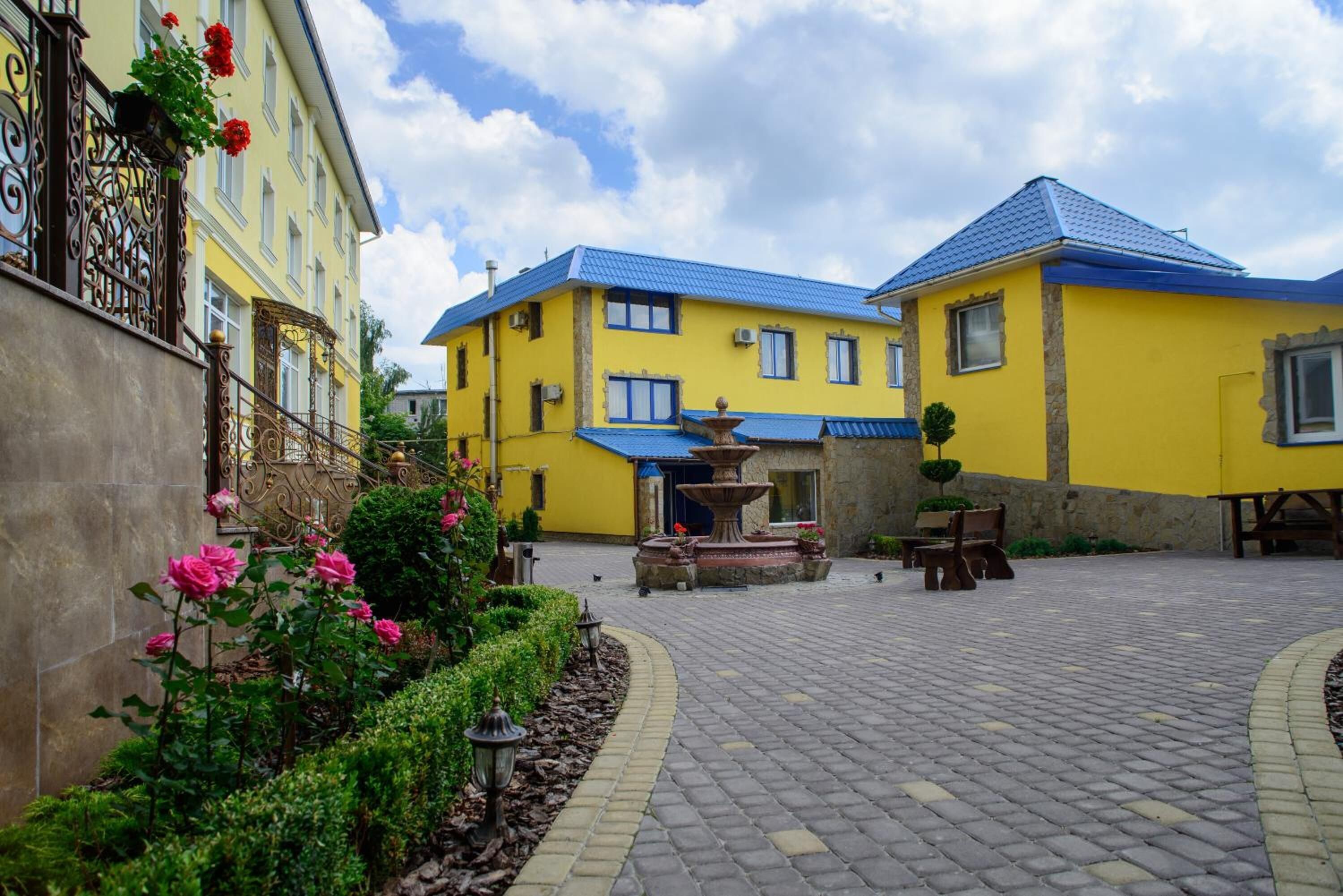 A courtyard with a fountain, benches, and a yellow building with blue roofing.
