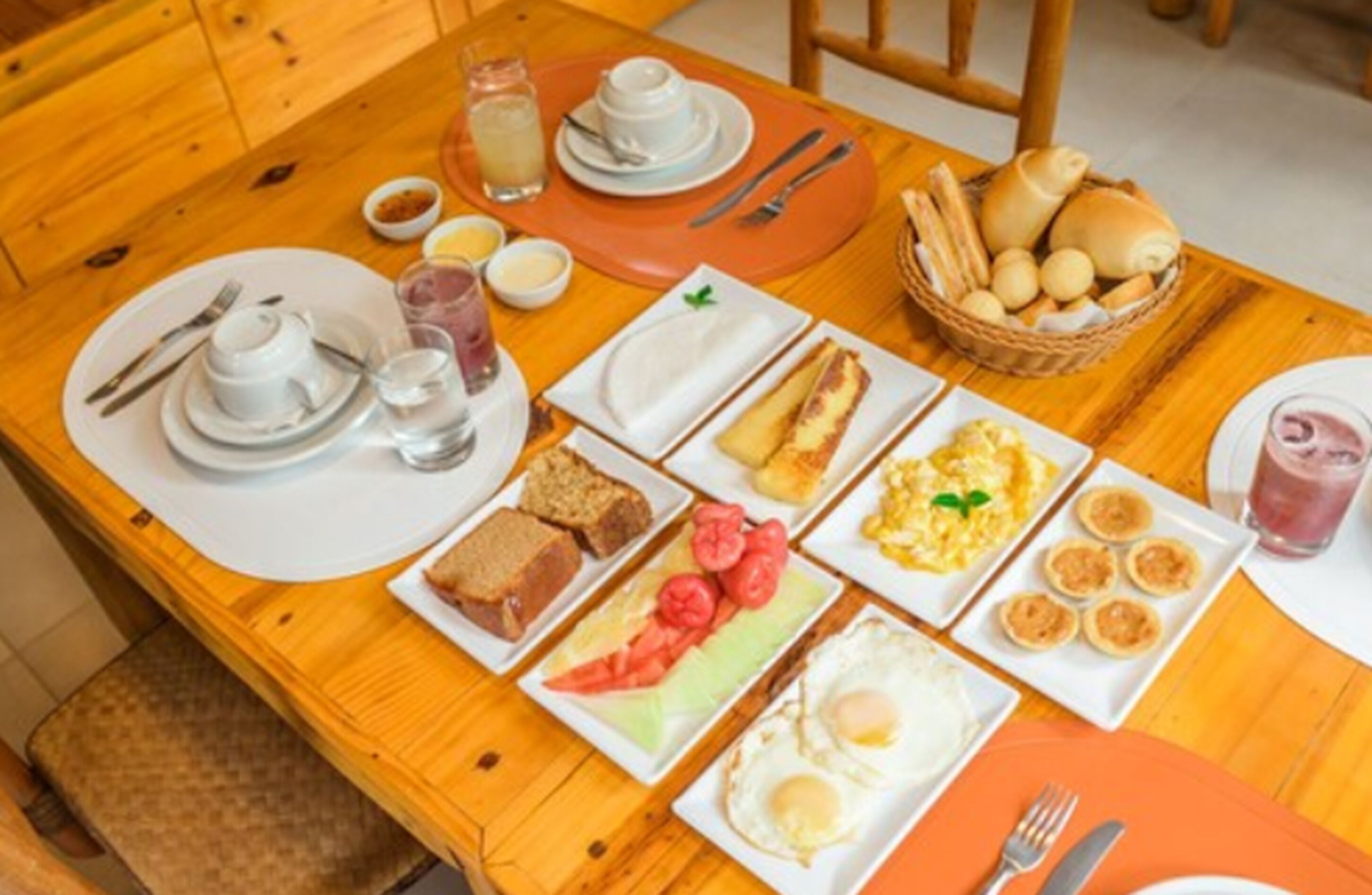 A breakfast setting with plates of toast, eggs, and pastries on a wooden table.