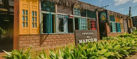 A building with colorful doors and windows, a sign reading "POUSADA do MAPCILLO," and a thatched roof.