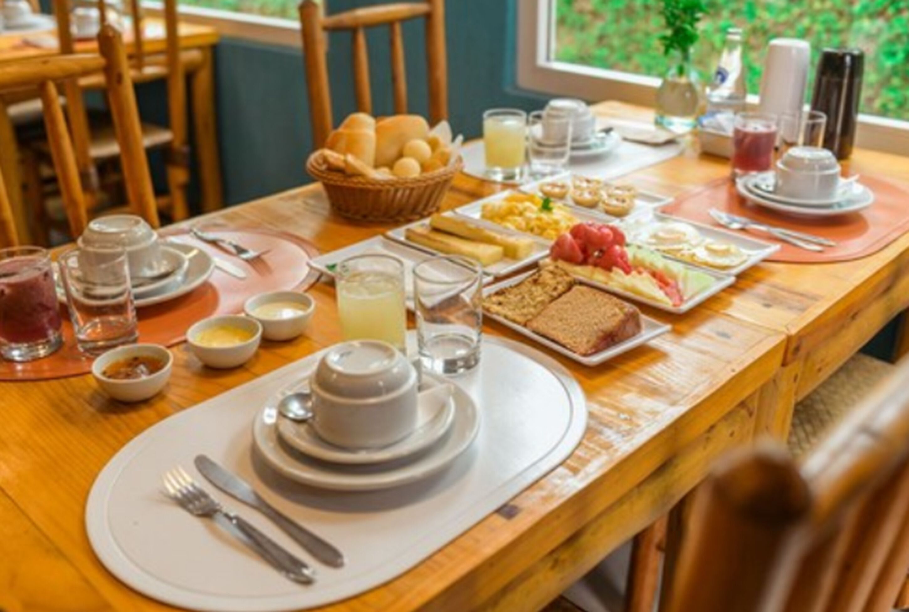 A breakfast setting with a wooden table, plates, bowls, and various food items.