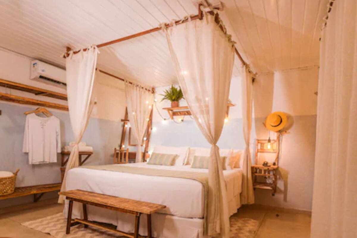Une chambre confortable avec un lit à baldaquin, un banc, une plante suspendue et un chapeau accroché au mur.