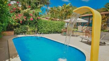 A swimming pool with a water feature, surrounded by lush greenery and a clear blue sky.