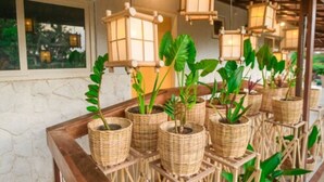 Des jardinières en osier, ornées de plantes vertes, sont posées sur une table en bois, sous des lanternes suspendues.
