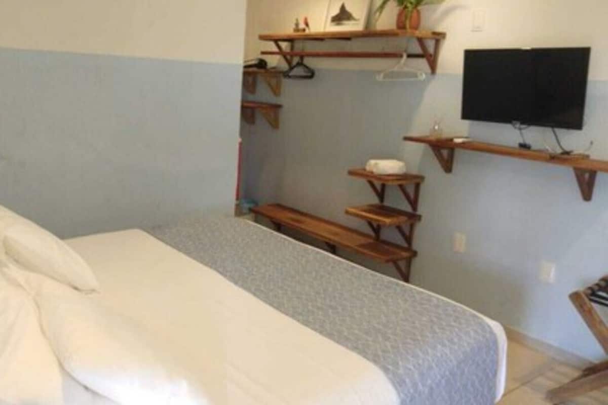 Ein Schlafzimmer mit einem Bett, einem an der Wand montierten Fernseher und einem kleinen Tisch mit Stuhl.