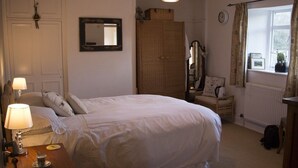 A bedroom with a bed, bedside table, lamp, wardrobe, mirror, and window with curtains.