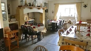 A dining area with multiple tables and chairs, a fireplace, and a window with curtains.