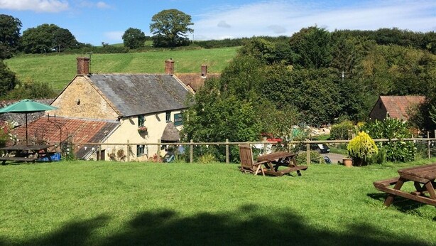 A rural setting with a stone building, picnic tables, and a fenced area.