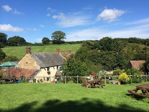 A rural setting with a stone building, picnic tables, and a fenced area. - The Mitre Inn (Sherborne)