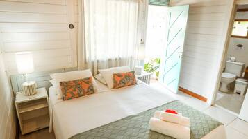 Quarto com cama, mesas de cabeceira, janela com cortinas e banheiro visível por uma porta aberta.