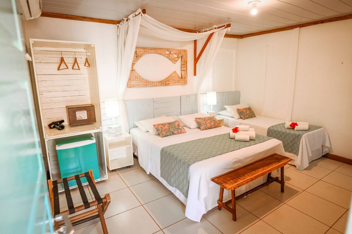 A room with two beds, a bench, a bedside table, a wall-mounted fish decoration, and a curtain.