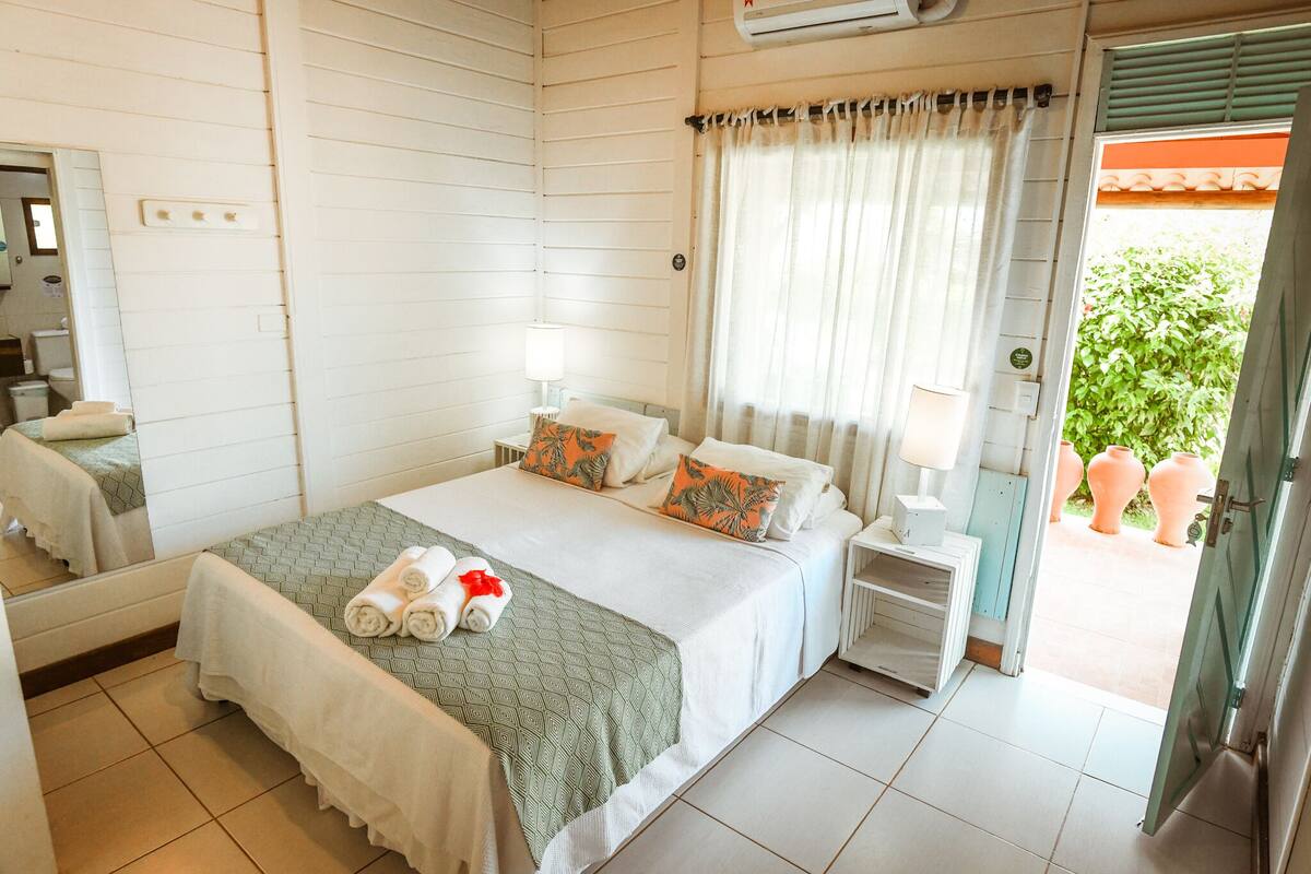 A hotel room with a bed, a nightstand, a mirror, and a window with curtains.