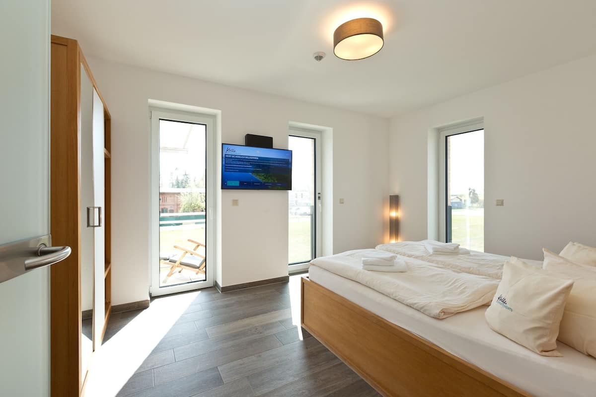 Ein modernes Schlafzimmer mit einem großen Bett, einem an der Wand montierten Fernseher und einer Glastür zum Außenbereich.