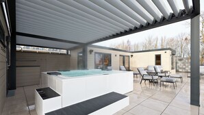 Moderni ulkoalue, jossa on poreallas, pergola, aurinkotuoleja ja taustalla kivimuuri.