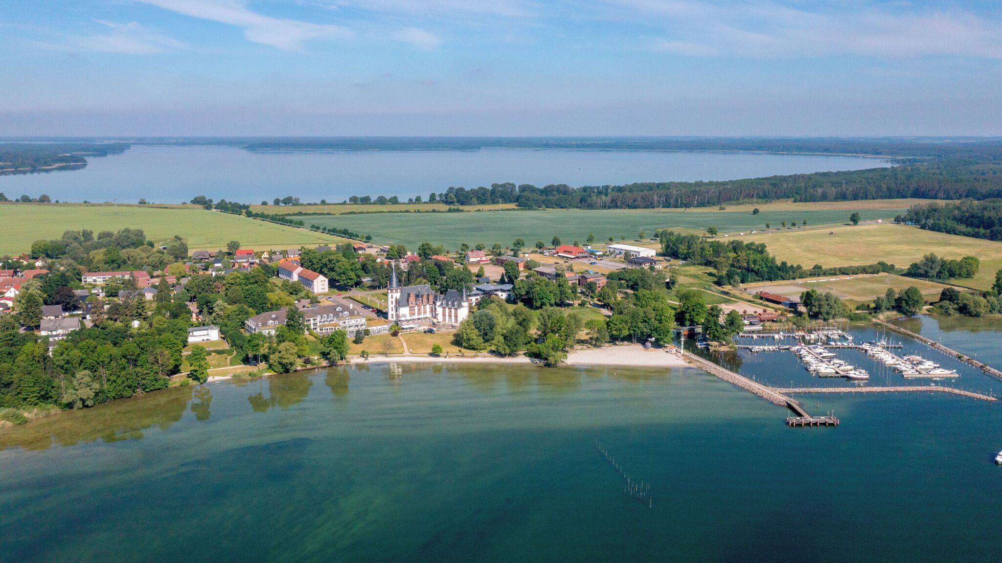 Luftaufnahme einer an einem See gelegenen Stadt mit einem Jachthafen, Wohngebäuden und offenen Feldern.