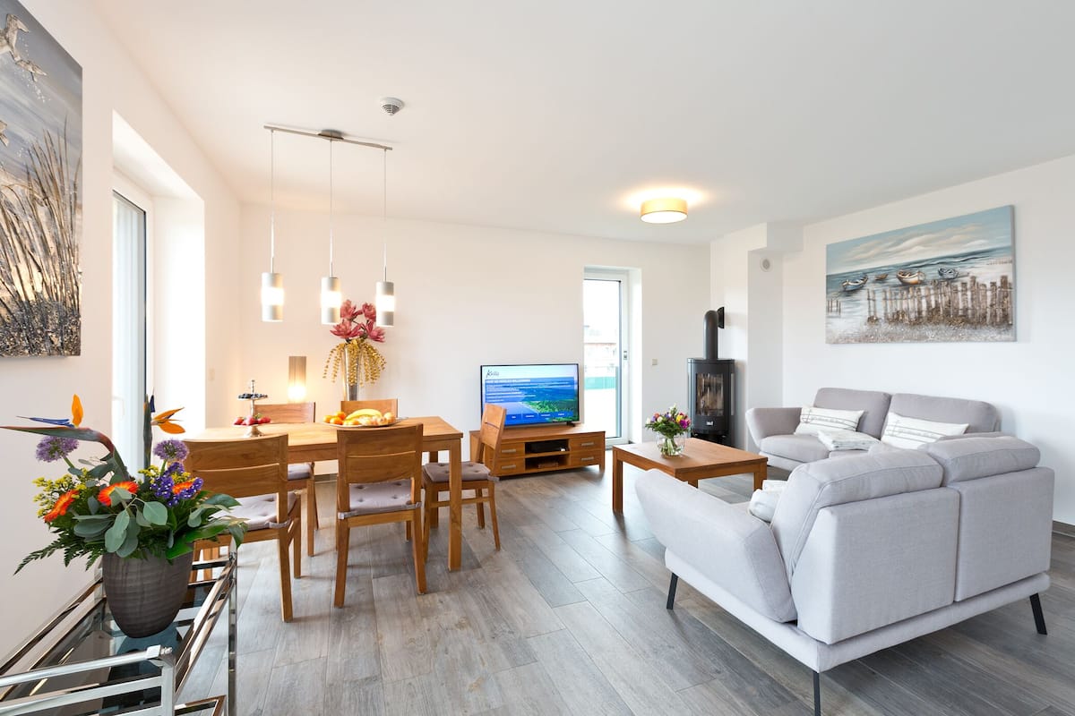 Ein modernes Wohnzimmer mit Sofa, Fernseher, Esstisch und Stühlen.
