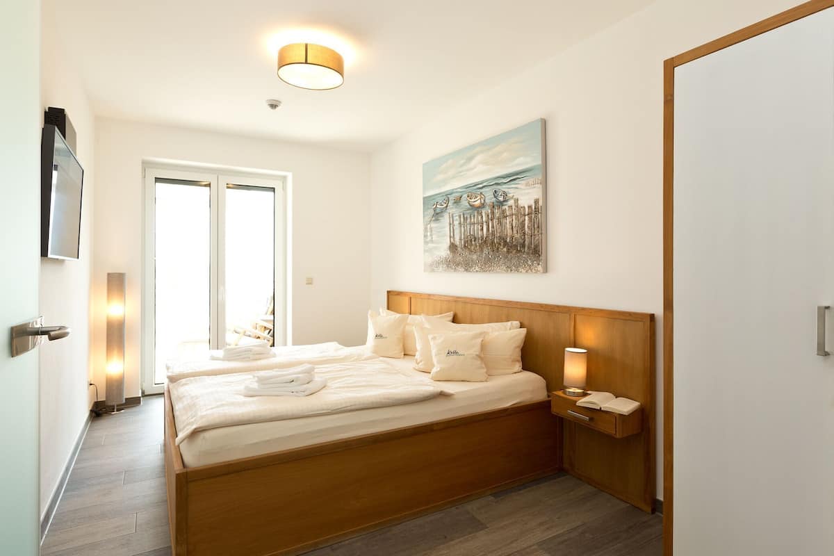 Ein Hotelzimmer mit einem hölzernen Bett, einem Nachttisch mit Lampe, einem Bild an der Wand und einer Tür, die nach draußen führt.