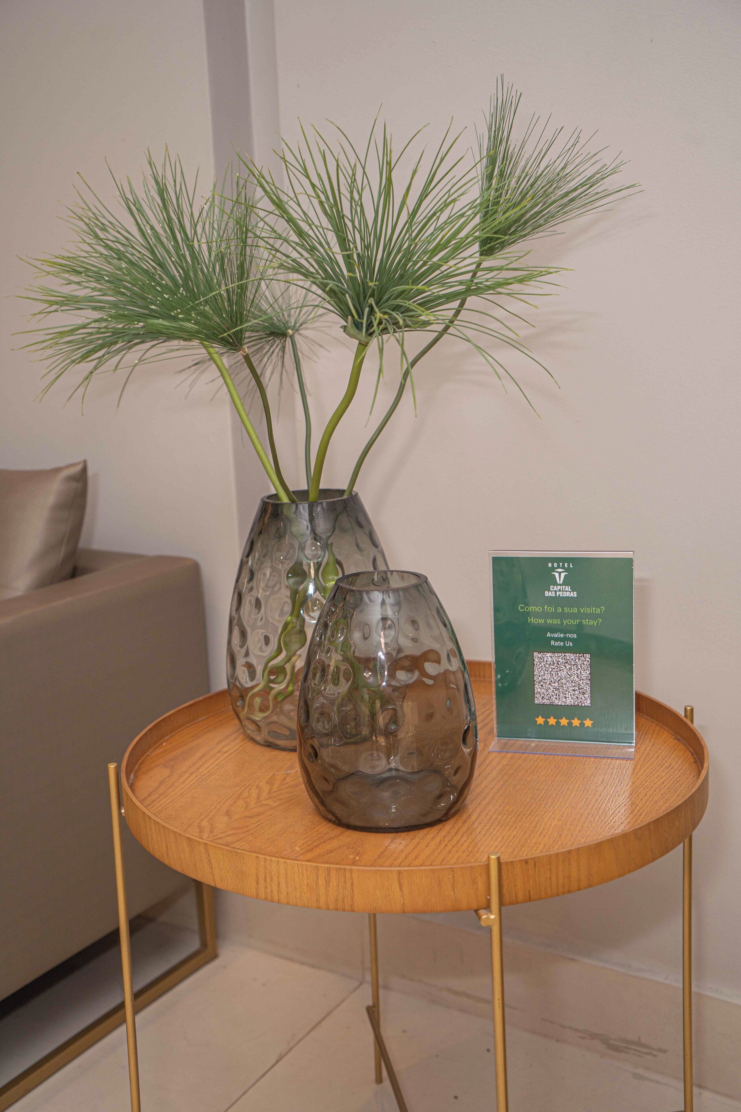 A round wooden table with two glass vases containing green plants and a hotel feedback card.
