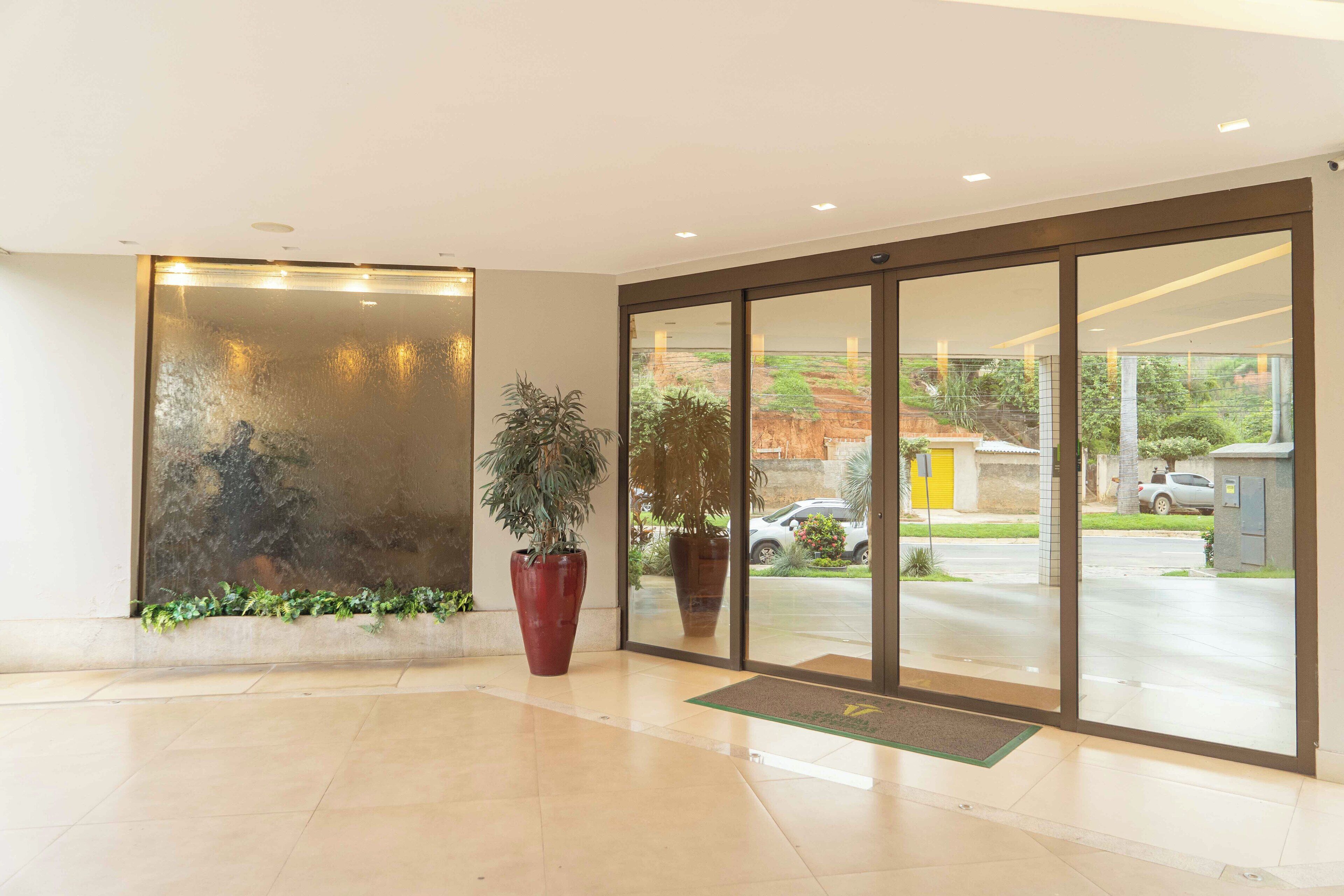 Un'accogliente hall d'hotel con un'ampia porta in vetro, piante in vaso e un pavimento piastrellato.