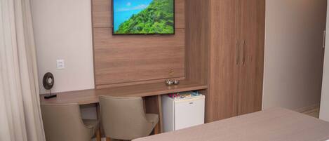 Ein Hotelzimmer mit einem Bett, einem Schreibtisch mit zwei Stühlen, einem an der Wand befestigten Fernseher und einer Minibar.