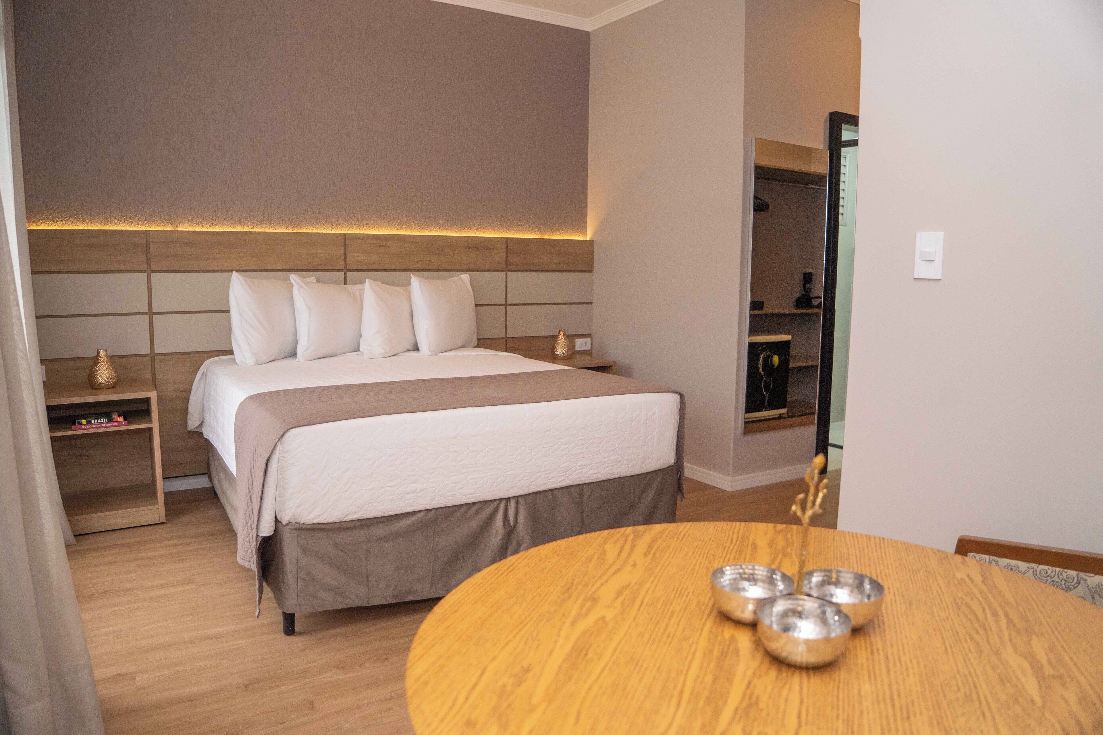 A hotel room with a large bed, bedside tables, a round wooden table with bowls, and a wardrobe.