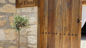 Une porte en bois avec une pancarte indiquant « Maison d’Eleni » et un pot de fleurs placé à côté.
