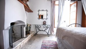 Une chambre à coucher avec un lit, une table de chevet, un miroir et une fenêtre avec des rideaux.