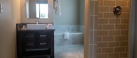 A bathroom with a dark vanity, a sink, a mirror, a towel rack, and a shower area with a tiled wall.