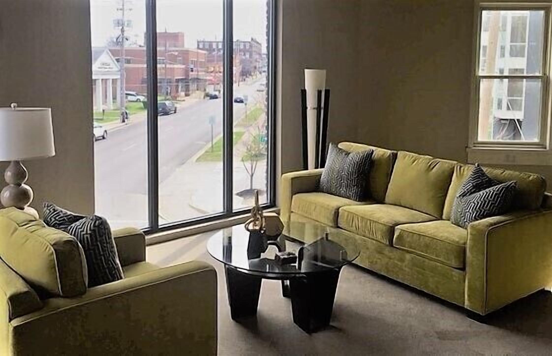 A modern living room with a sofa and armchair facing a large window, a glass coffee table, and a floor lamp.