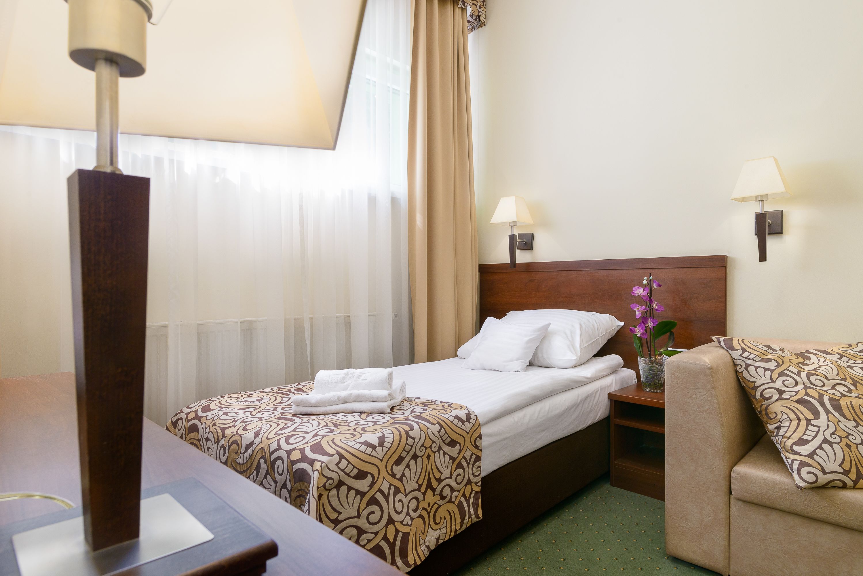 Een hotelkamer met een bed, nachtkastjes, lampen en een kleintje tafeltje met een bloevas.