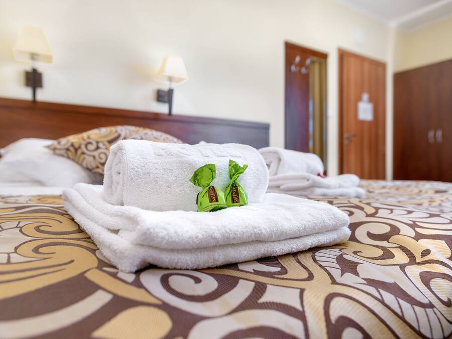 Una cama bien hecha con toallas blancas dobladas y una bolsa de regalo verde encima.