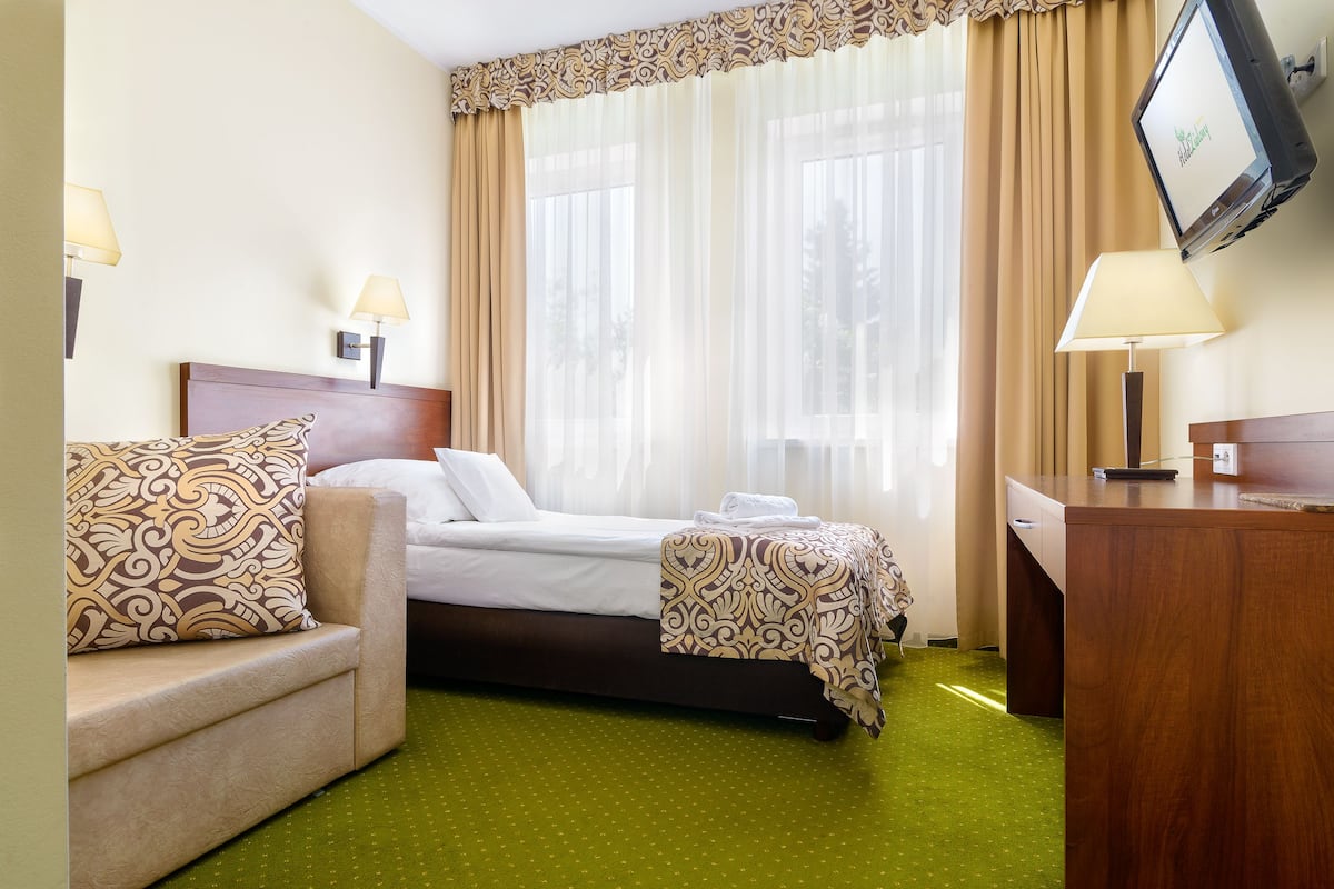 Quarto de hotel com cama, escrivaninha, cadeira e televisão.
