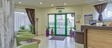 A hotel lobby with green seating, a reception desk, and a green door.