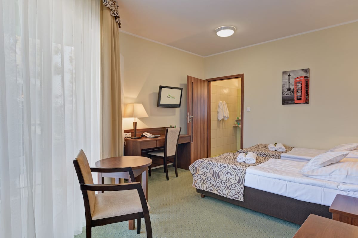 Quarto de hotel com cama, escrivaninha com cadeira, abajur e quadro com uma cabine telefônica vermelha na parede.