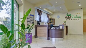 A hotel reception area with a reception desk, a clock, and a sign for Hotel Zieleny. - Hotel Zielony (Poznan)