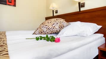 A neatly made bed with white linens, a patterned pillow, and a single rose.