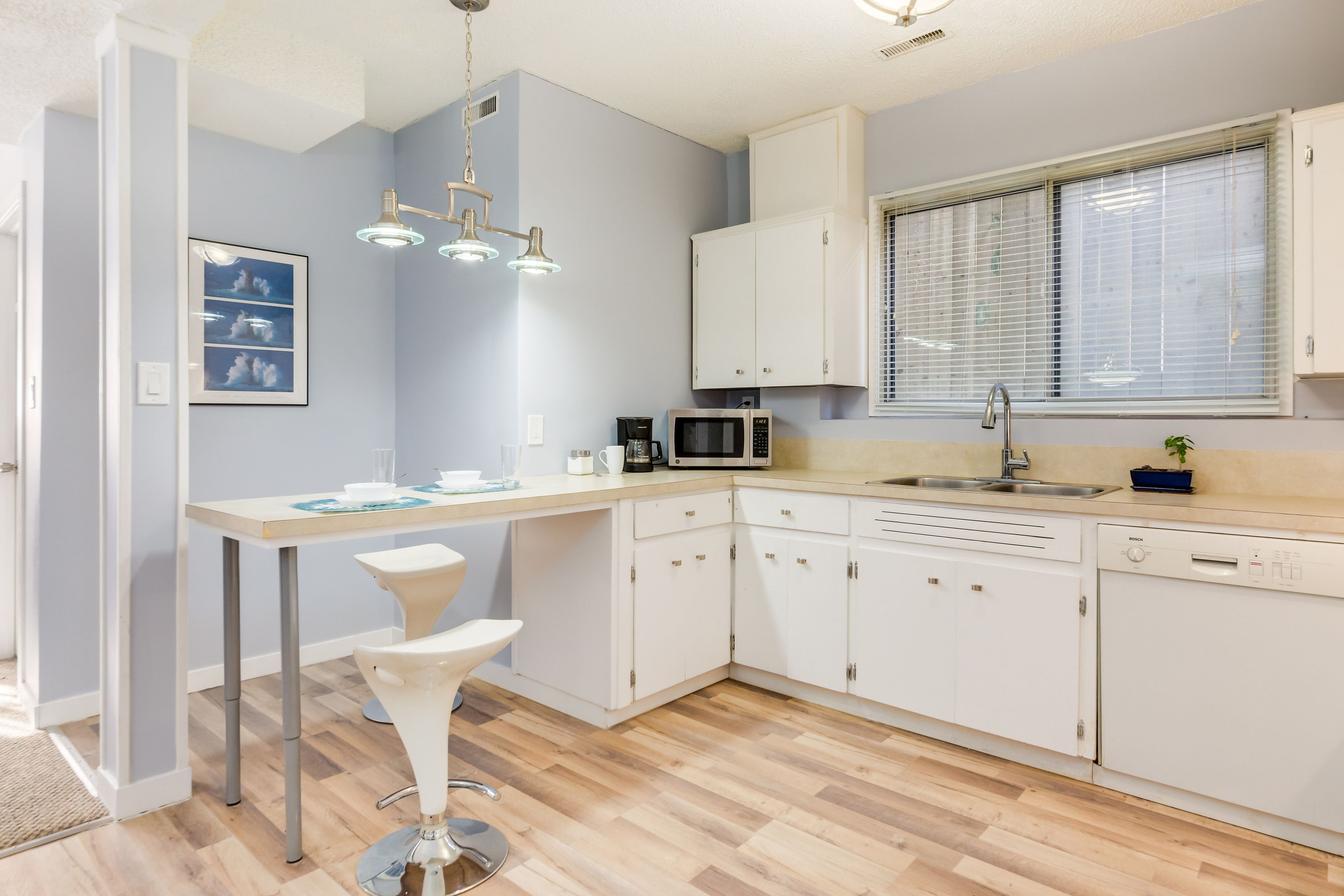 A modern kitchen with white cabinets, a microwave, a sink, and a dining area with a white chair.