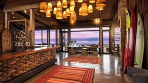 A spacious bar area with a view of the ocean, wooden ceiling, and surfboards on display. - Hotel Alaia (Pichilemu)