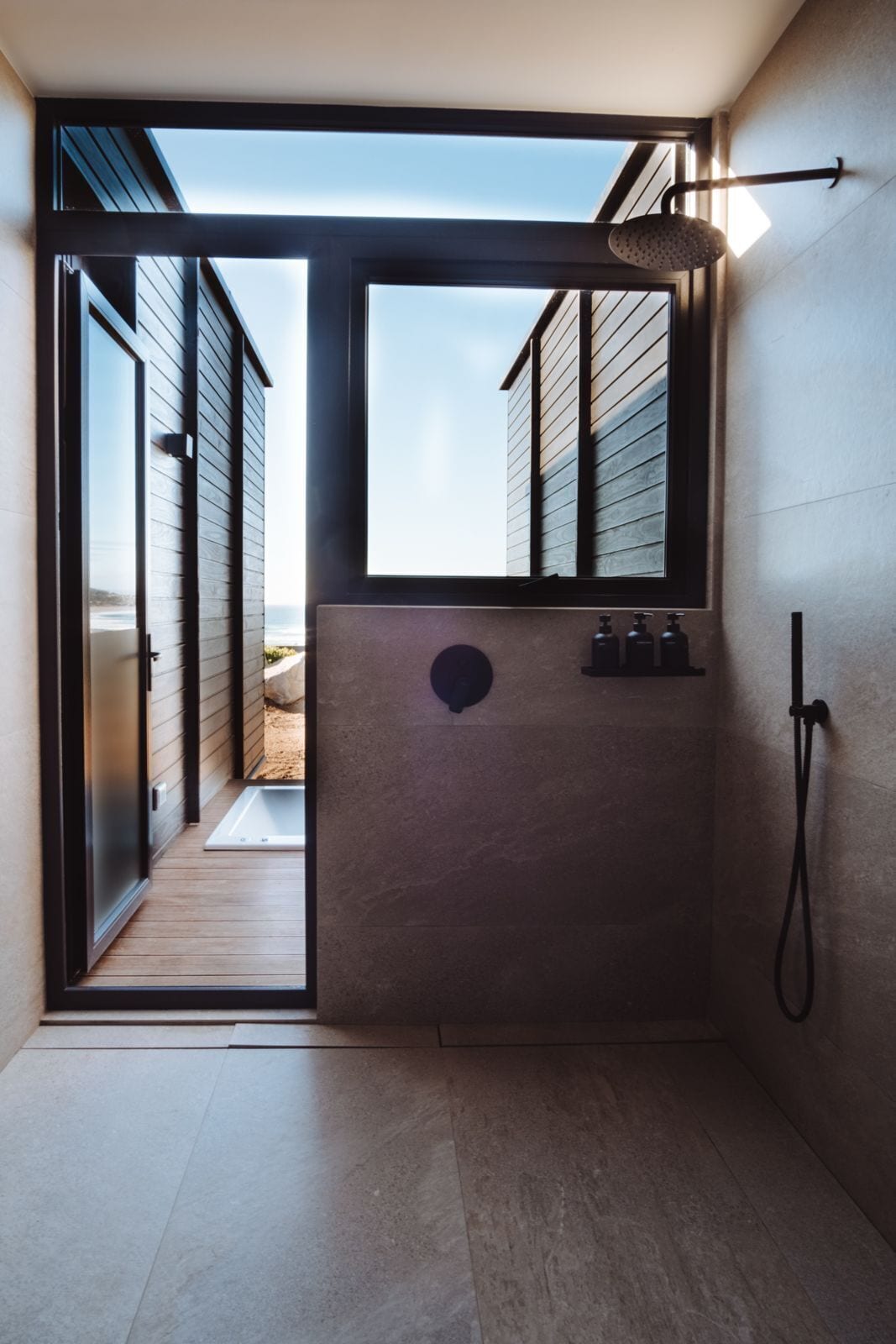 A modern bathroom with a large window, a shower area, and a visible outdoor view.
