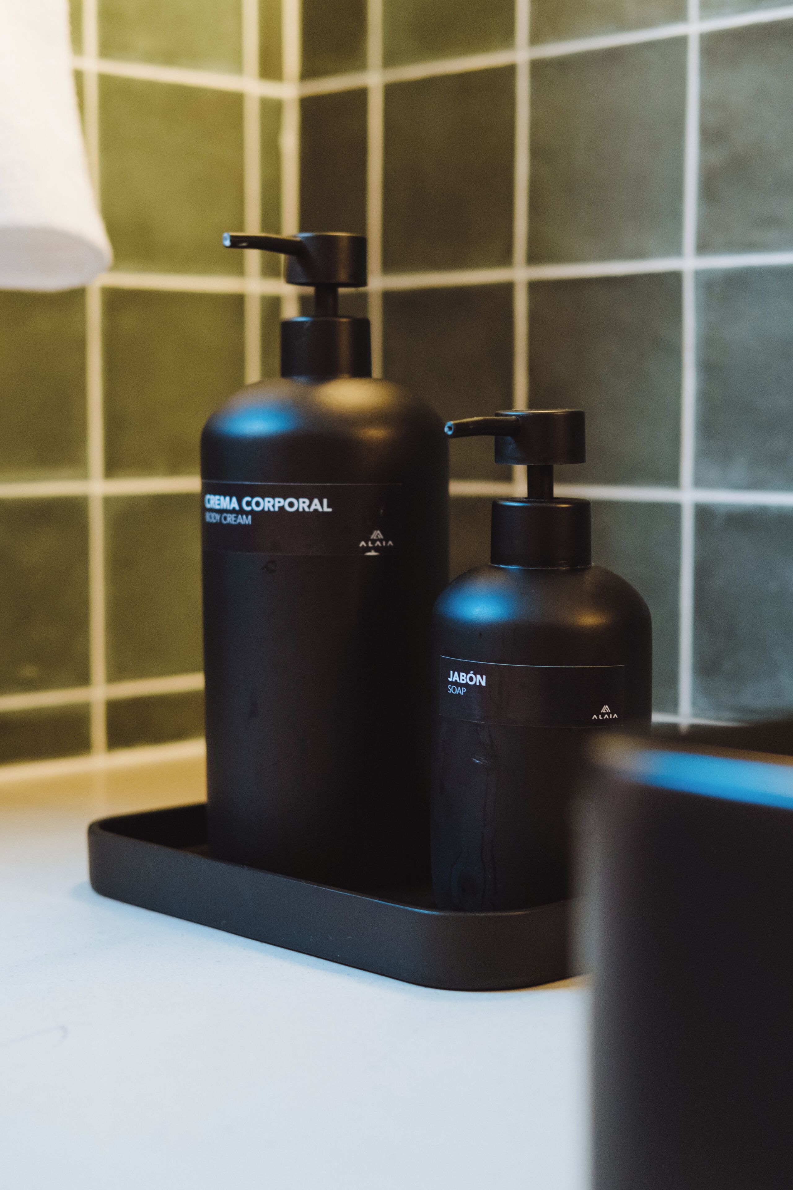 Dos botellas negras de artículos de aseo sobre una bandeja en un baño con paredes de azulejos verdes.
