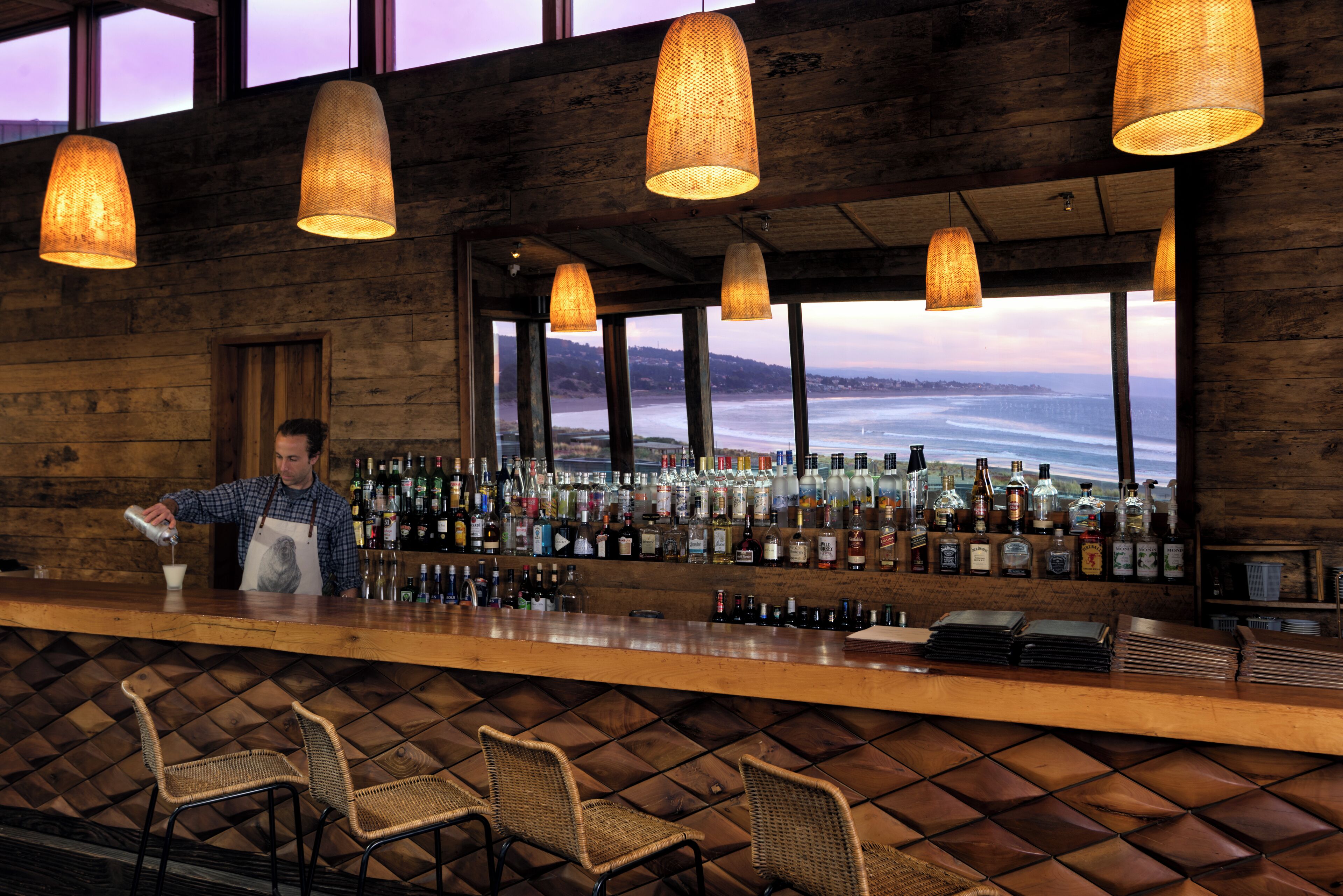A bar with wooden walls, wicker chairs, and a view of the ocean.