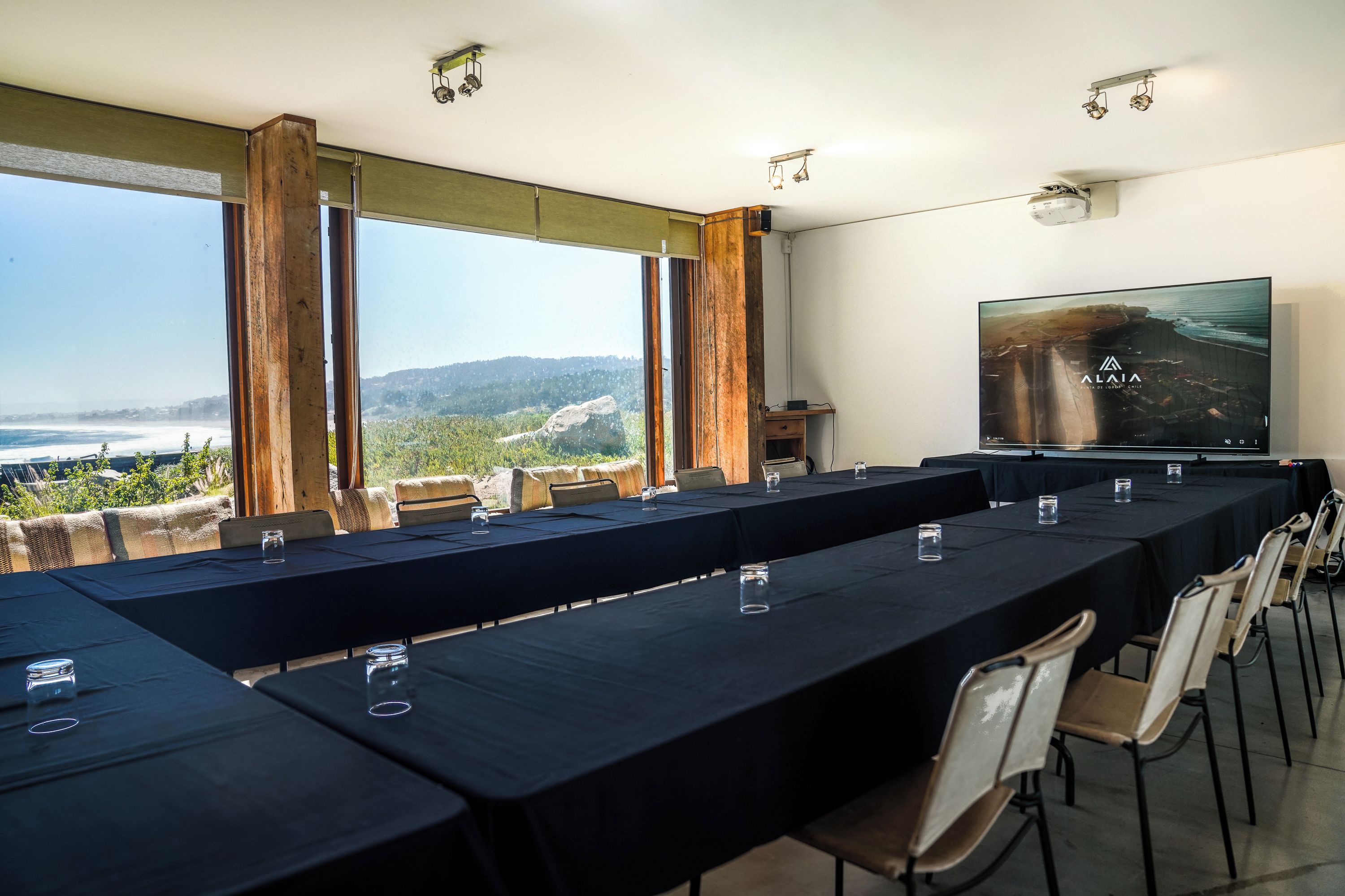 A conference room with a long table, chairs, and a large screen displaying a landscape.