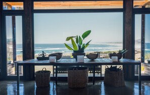A room with a large window overlooking a beach, a wooden table with baskets and a plant, and a sculpture. - Hotel Alaia (Pichilemu)