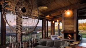 A cozy living room with a large window, a fireplace, and a hanging net structure. - Hotel Alaia (Pichilemu)