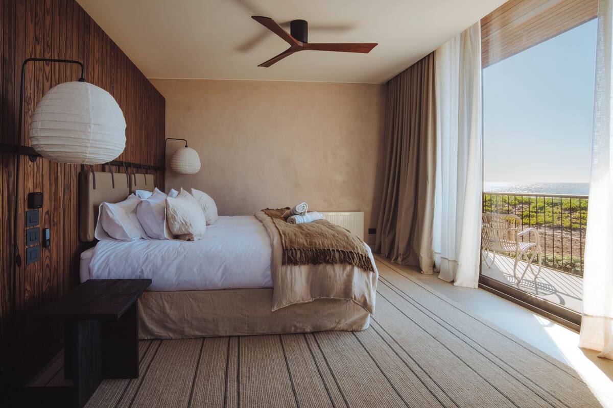 A bedroom with a bed, a ceiling fan, a nightstand, and a view of the outdoors.