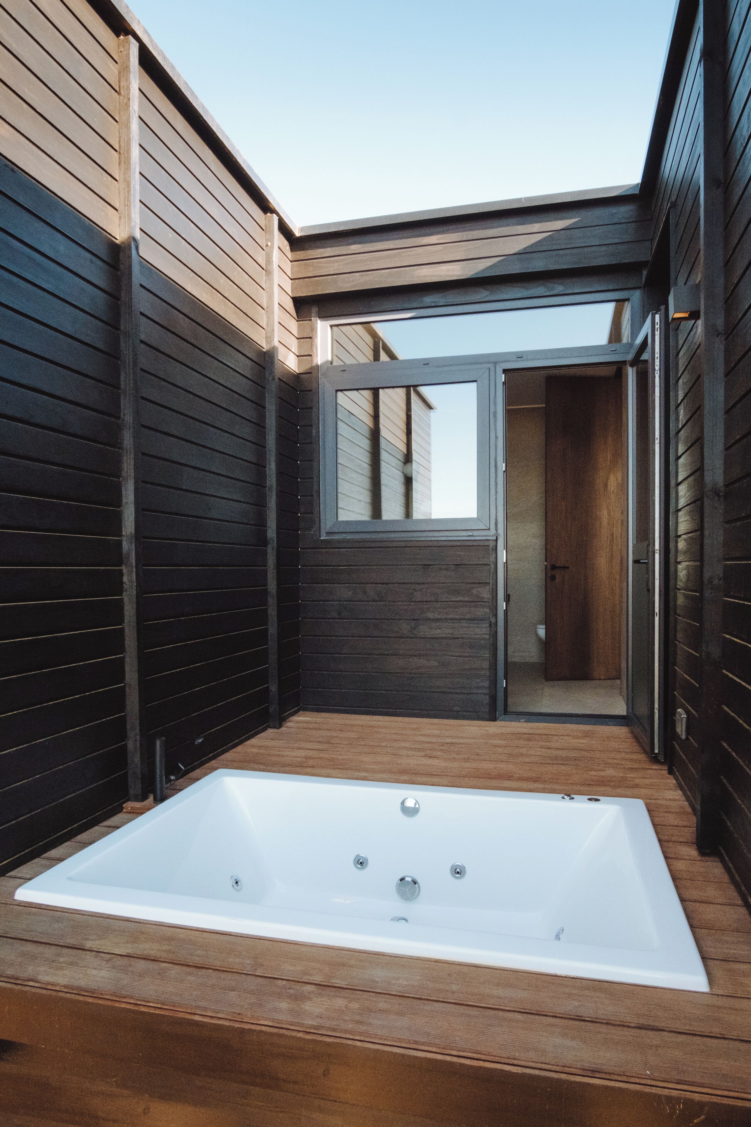 Un área de spa con una bañera blanca grande, una terraza de madera y una puerta que da al baño.