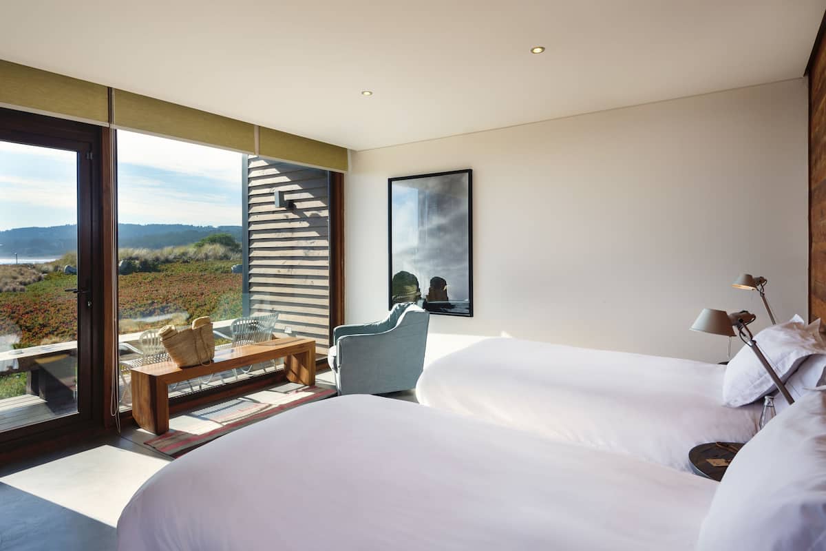 A modern hotel room with a large bed, a seating area with a view, and a staircase leading to an outdoor terrace.