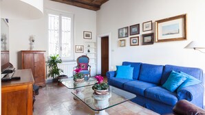 A living room with a blue sofa, a glass coffee table, a wooden cabinet, a chair, and a potted plant. - Habitat's Campo di Fiori Apartments (Rome)